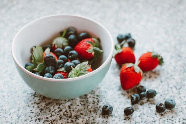 Bowl of fresh mixed berries with a few berries scattered around it, illustrating polyphenol-rich fruits that help support a diverse and healthy gut microbiome.