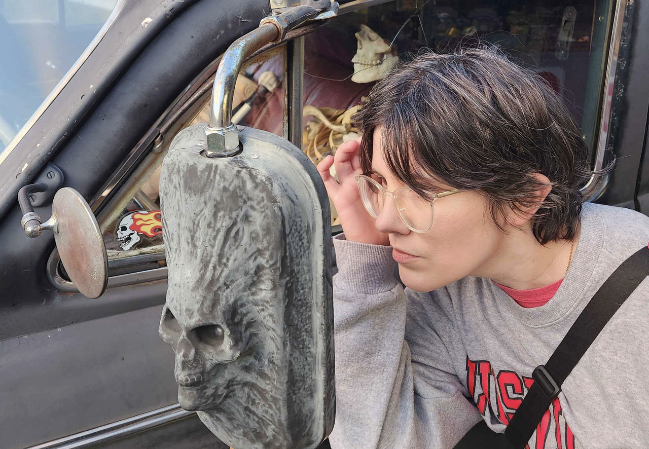 Mel looking into the rear-view mirror of a skeleton car