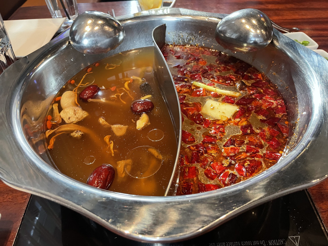 A pot that is split down the middle, with mushrooms in a brown broth on the left and a red and brown-yellow broth on the right.