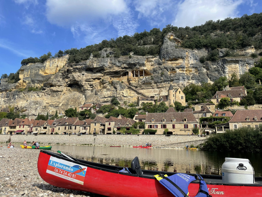 A photo of a red canoe with a village in the background, which is La Roque-Gageac.