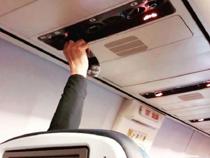 Penumpang mengeringkan kaus kaki di ventilasi udara pesawat.