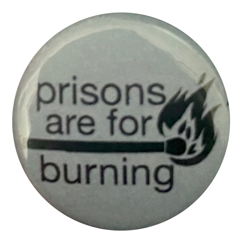 a light blue pin that says 'prisons are for burning' with a match on fire at the end in between 'are for' and 'burning'