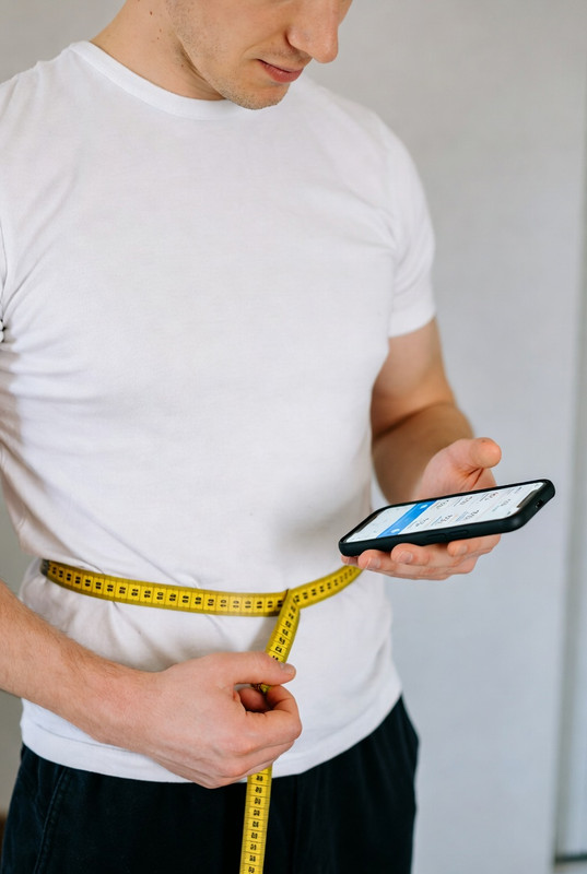 Person measuring waist and logging data on a fitness app.