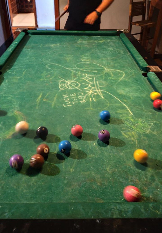 visão de uma mesa de sinuca, ponto de vista de quem está jogando. do outro lado da mesa tem uma pessoa, só aparece a cintura