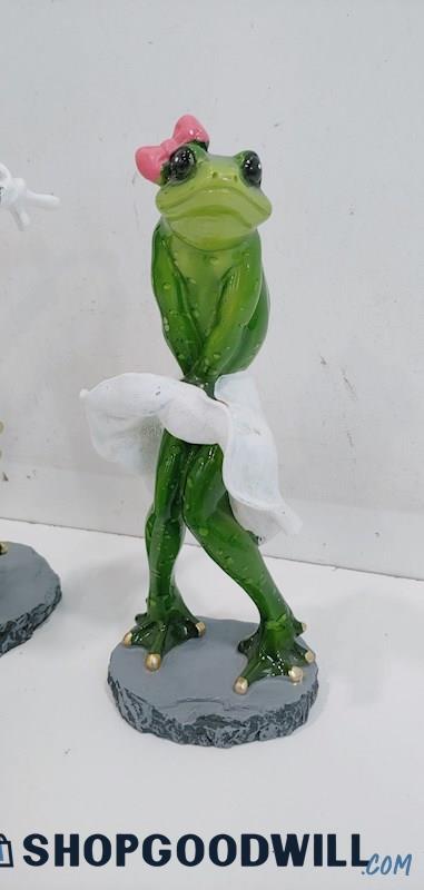 a product photo of a statue of an upright frog in the famous Marilyn Monroe blowing-skirt pose. the frog is wearing only a billowing white skirt and a bright pink bow.