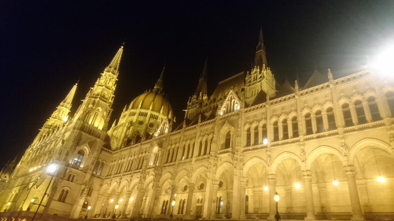 Picture of the Hungarian parliament at night. It is a neo-gothic building. In this photo, there is one dome, just left of the centre, and three towers.
