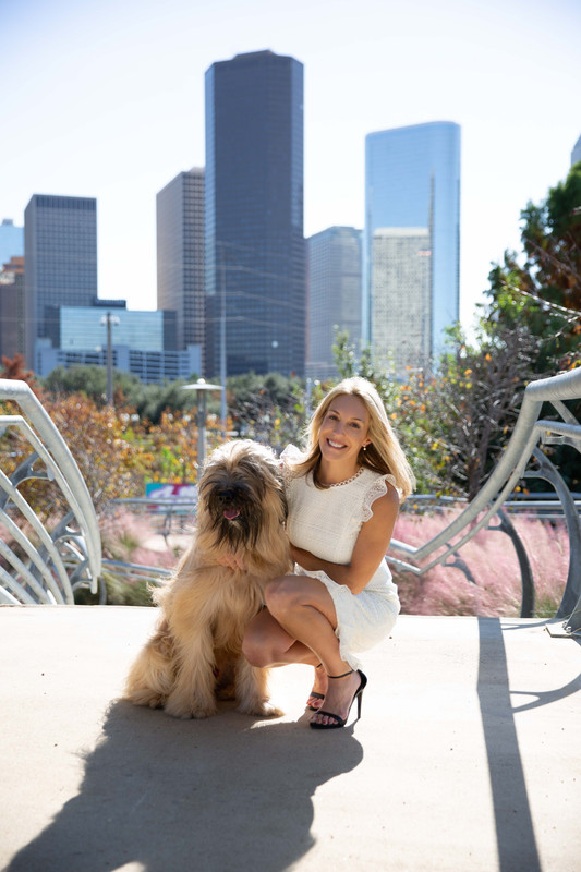 The caption for the given image is A woman sitting on a sidewalk with a dog.