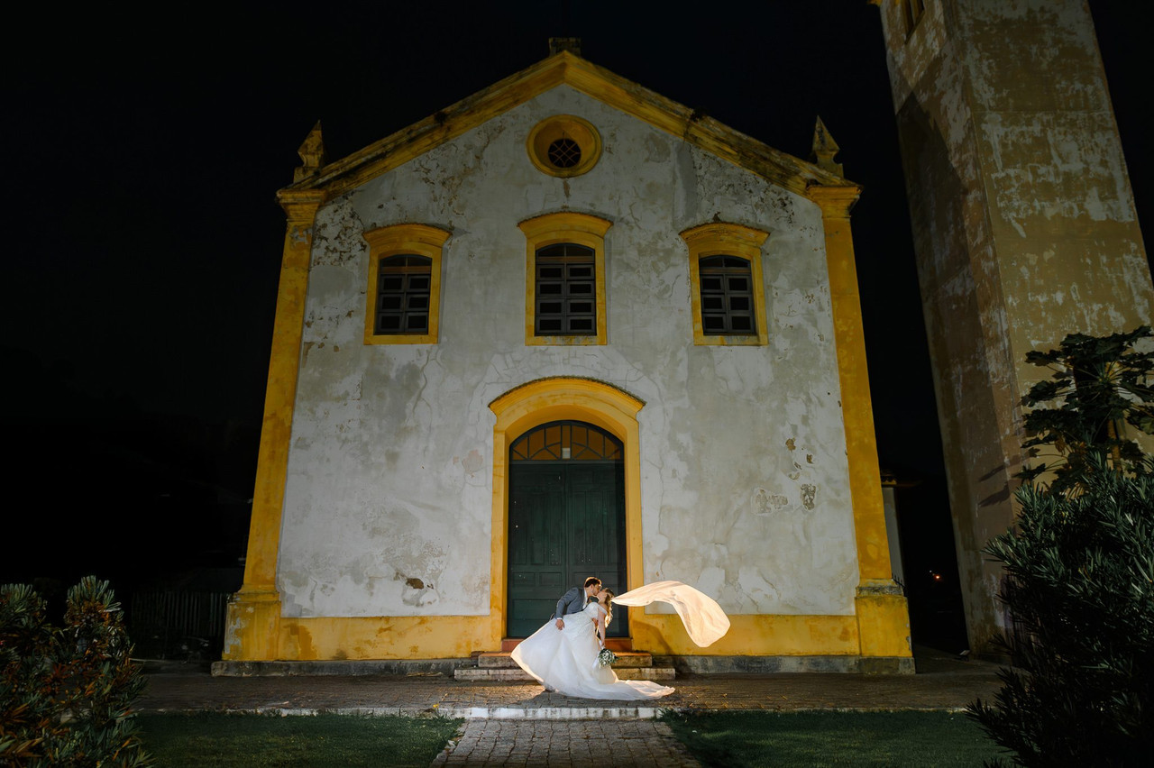 Noiva diante de igreja histórica com véu em movimento