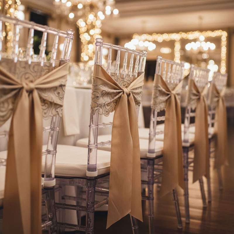 Элегантные дизайнерские стулья с элементами кастомизации, украшенные декоративными лентами и текстилем, в интерьере праздничного зала.