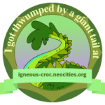 small 150x150 circular badge with a picture of the website owner's handsome tail. The text reads I got thwumped by a giant tail at igneous-croc.neocities.org