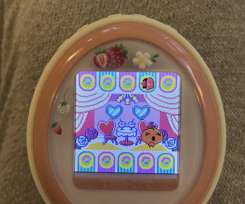 close up photograph of a tamagotchi plus color device. memetchi is waiting for her surprise date, picked by the matchmaker, and looking excited