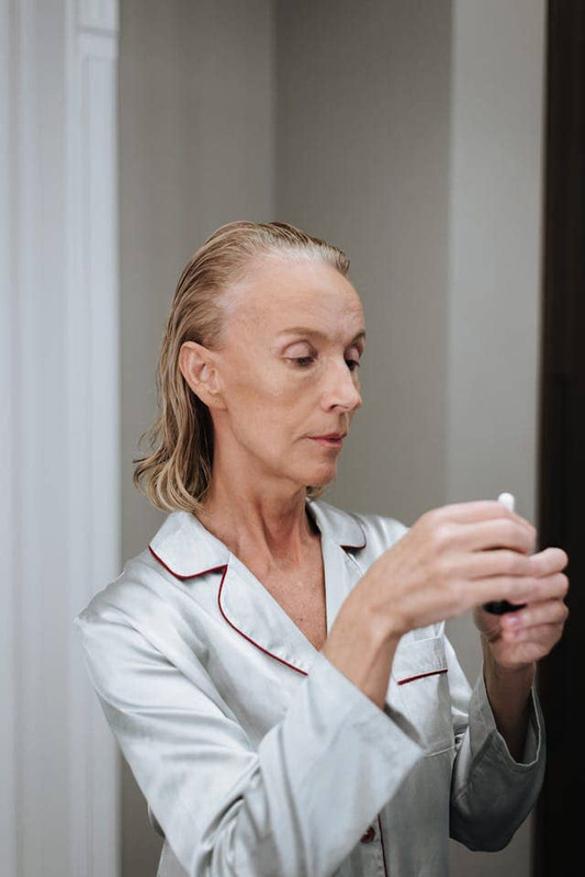  an elderly woman applying anti-aging ingredients on her skin. 