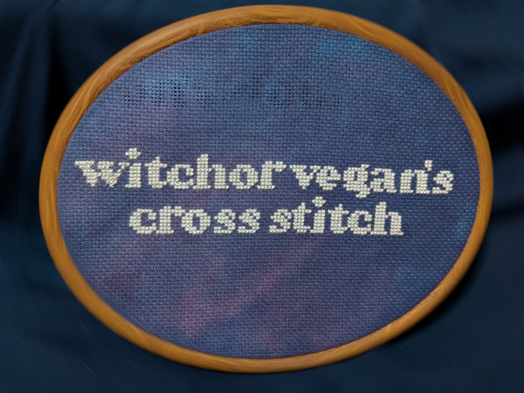 The words 'witchorvegan's cross-stitch' cross-stitched in white onto dark blue fabric.