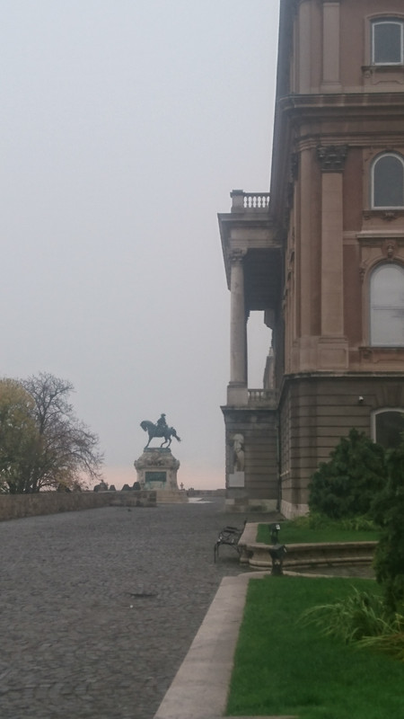 Pink dawn rising behind statue of a rider on a horse, next to a Rococco building.