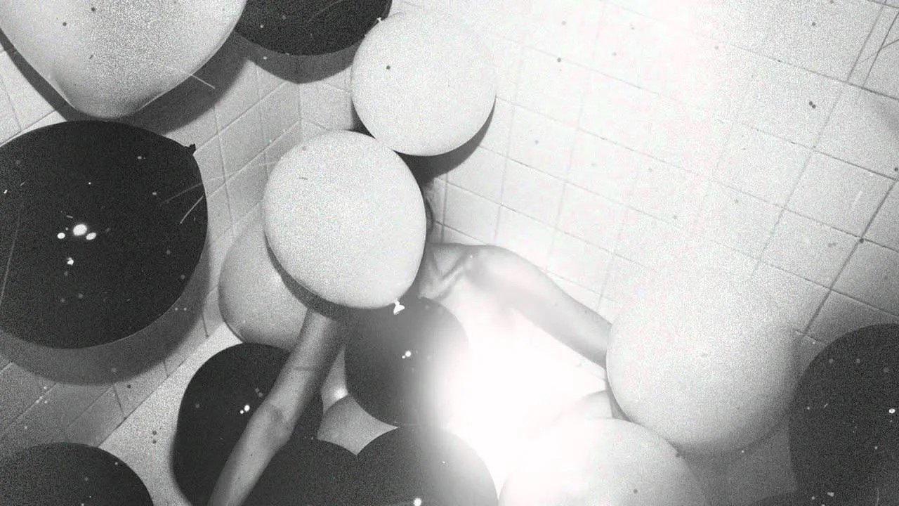 A grainy, high-contrast photo of a person's hands amidst white and black balloons.
