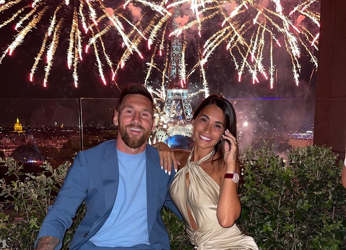 Lionel Messi dan Antonela Rocuzzo berpose dengan latar keindahan Menara Eiffel di Paris saat malam hari.