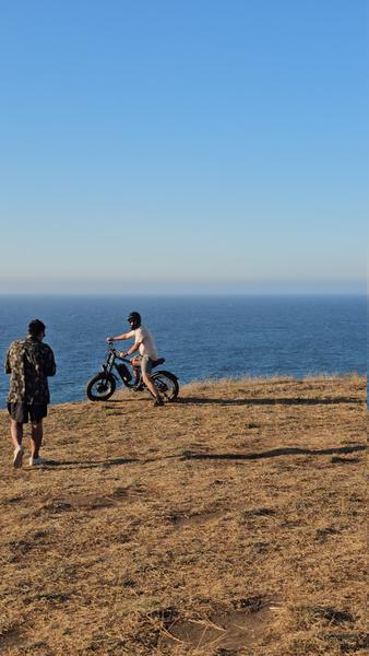 Guía y ciclista en e-bike en lo alto de un cerro con el océano Pacífico de fondo