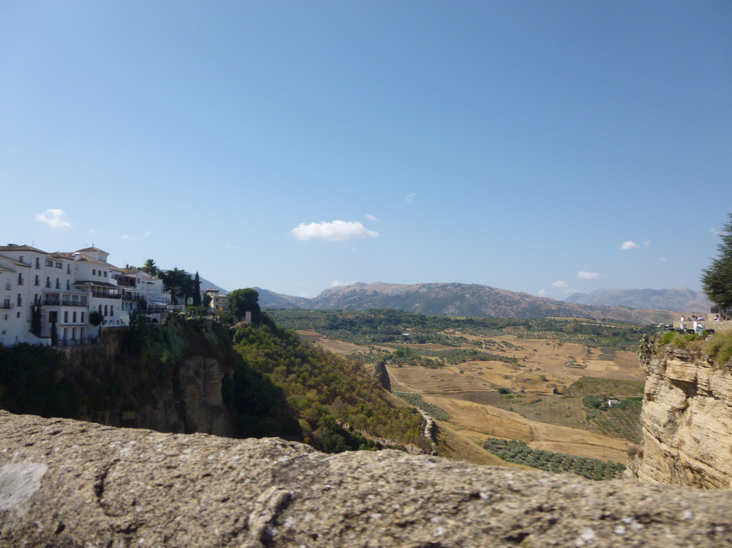 View from the "New Bridge" (built 1751) which joins the two towns.

The bridge stone which is at the bottom of the picture is grey.  On the left hand side are small white houses, there is a view over the plain the town is on (with fields of what might be olive trees), then the white of the other side of the gorge.