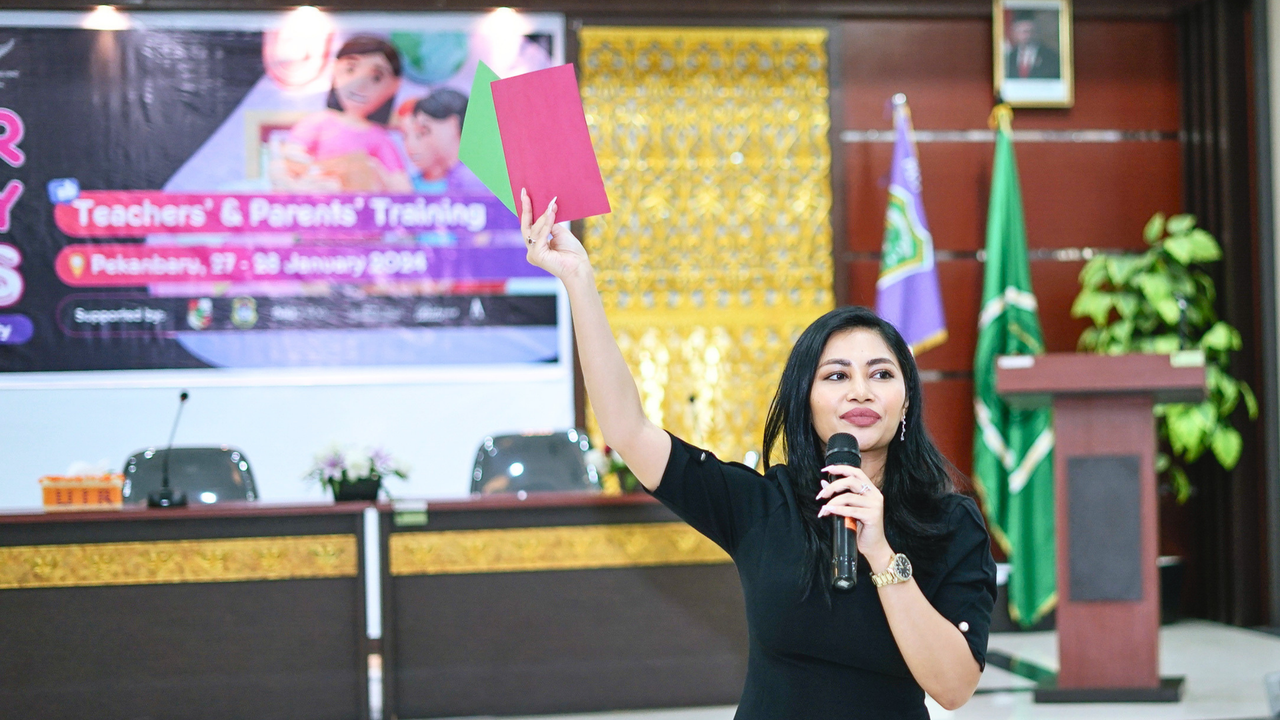 Teachers in batik and hijab holding a training certificate on stage