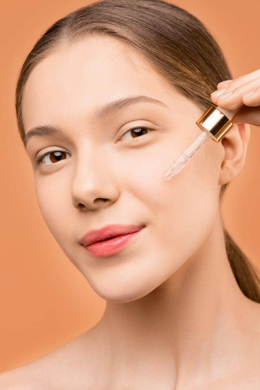 Woman applying vitamin C serum on her face, showing daily skincare to restore vitamin C levels in the skin.
