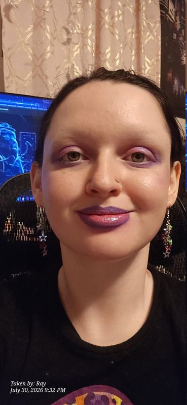 A selfie of my makeup with the lisa frank shirt and star earrings. I have a light and bright pink eye shadow on my lids and a light bright purple shadow under my lower lashline and smoked out of my outer corner blended into the pink. My lips are lined in a purple that matches the purple on my shirt and my eyeshadow and the inner part of my lips is the same shade of bright pink. both my lips and my eyes have a very light blue shimmer applied but it doesn't show up very well in the picture. It's hard to describe to a person who cannot see but the colors in my makeup match colors used in the shirt design almost perfectly.