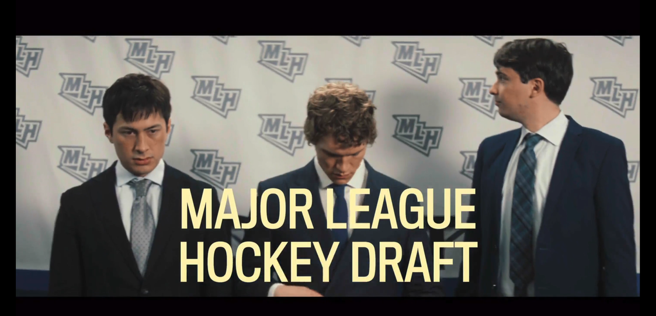 "major league hockey draft" overlays the screen in yellow all caps. shane, ilya, and a third young man stand in suits in front of an MLH branded wall. shane is wearing a standard suit: white shirt, black jacket, and a silver tie with a diagonal grid pattern. ilya is wearing a dark, navy blue suit jacket, white shirt, and dark blue tie. the third young man is wearing a dark blue suit jacket and green and blue tartan tie. 