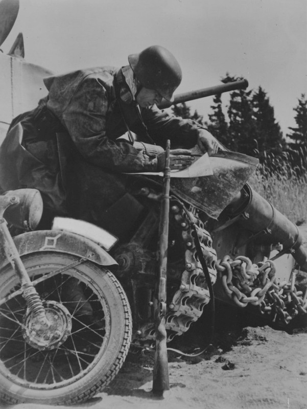 Немецкий мотоциклист изучает карту рядом с советским танком Т-26.