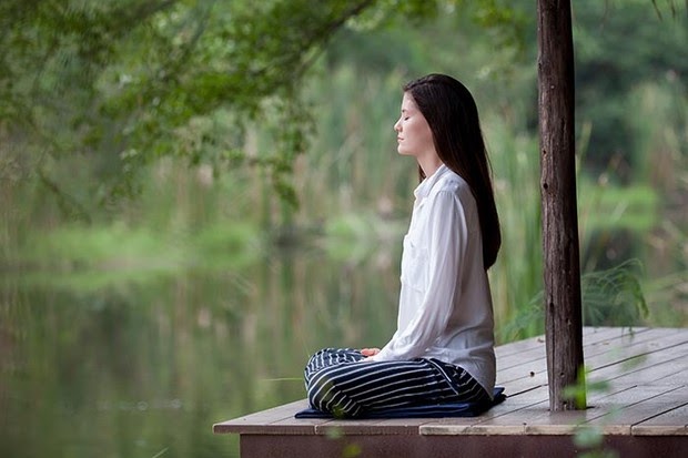 Devojka meditira na tremu pored jezera