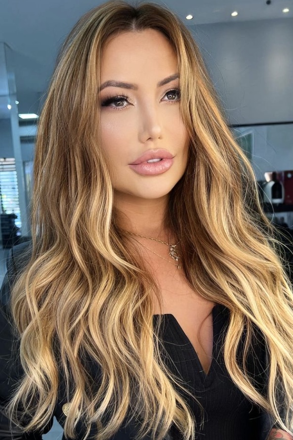 A girl with full lips, brown eyes and dark hair dyed in warm honey balayage