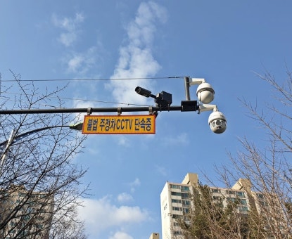 Fixed illegal parking enforcement CCTV camera pole with a yellow warning sign in Korea