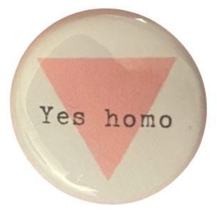 a white pin with an upside down pink triangle on it that says 'Yes homo' in courier new font in front