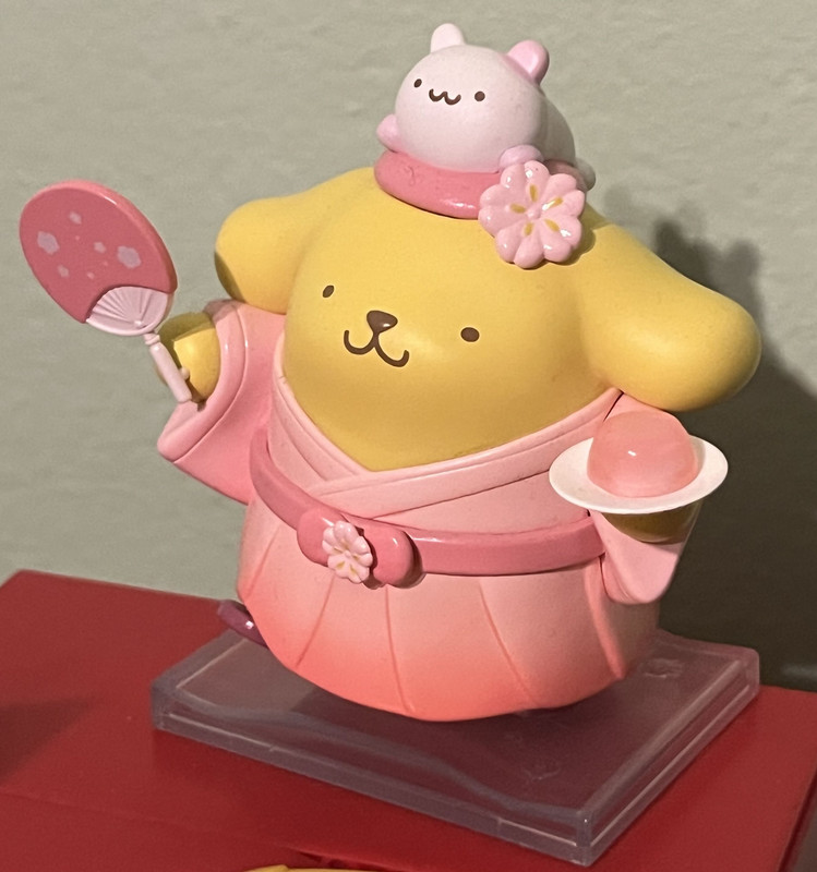 A figure of Pompompurin, a yellow cartoon dog, in a pink outfit