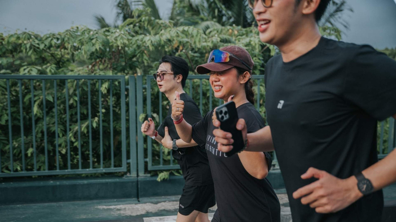 Runner cầm điện thoại theo dõi số liệu chạy bộ trong buổi tập nhóm ngoài trời"