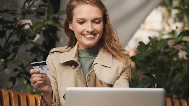 young cheerful woman with credit card checking her bank account laptop using free internet connectio