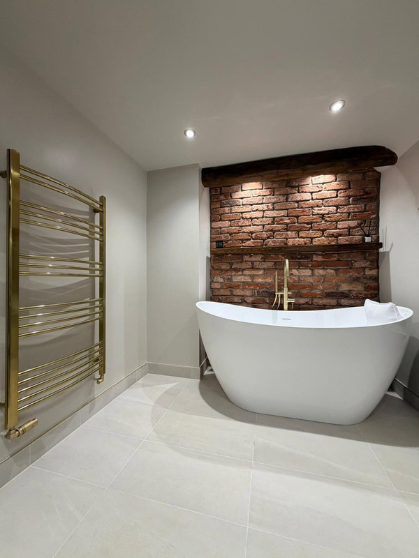 Freestanding bath with exposed brick feature wall and brass towel rail