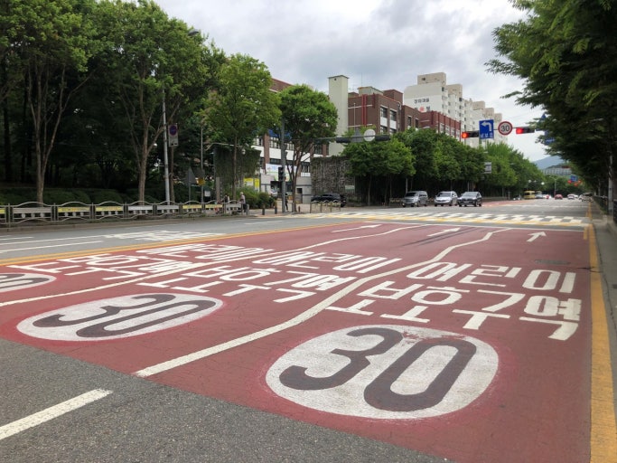 Red-painted school zone road surface in Korea with a 30 km/h speed limit painted twice on the pavement