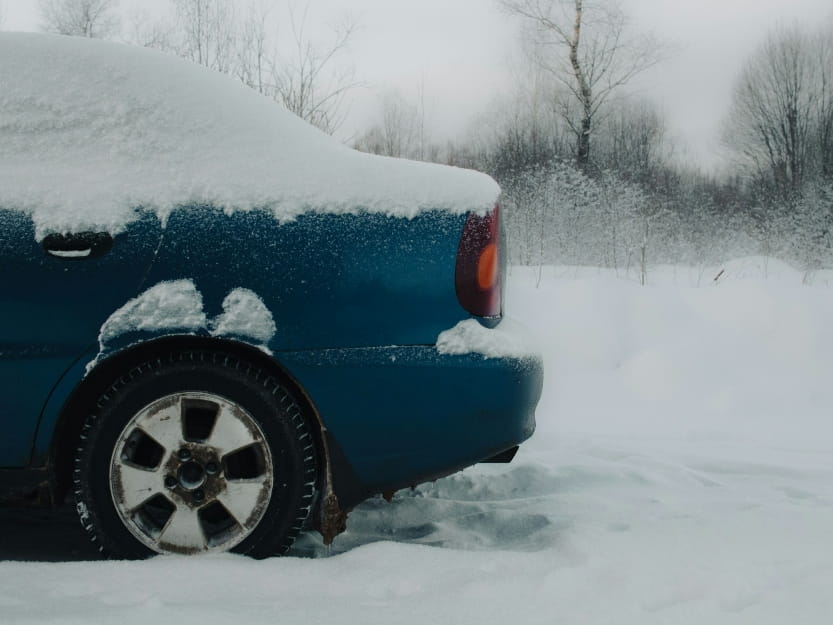 rear side of a snow-covered car showing tire and wheel in winter conditions