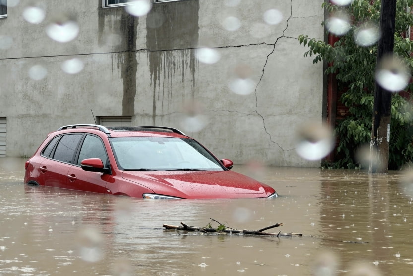Red SUV submerged in floodwater up to its windows during a heavy rainstorm