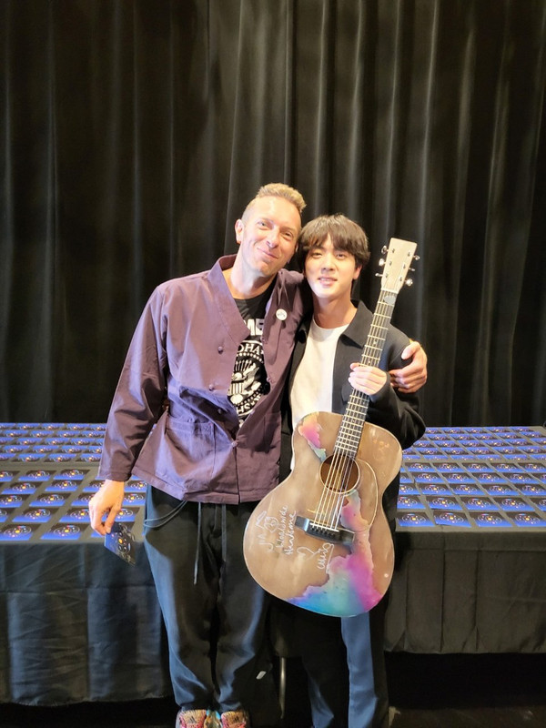 Jin BTS (kanan) berfoto dengan Chris Martin sambil membawa gitar hadiah dari vokalis band Coldplay tersebut.