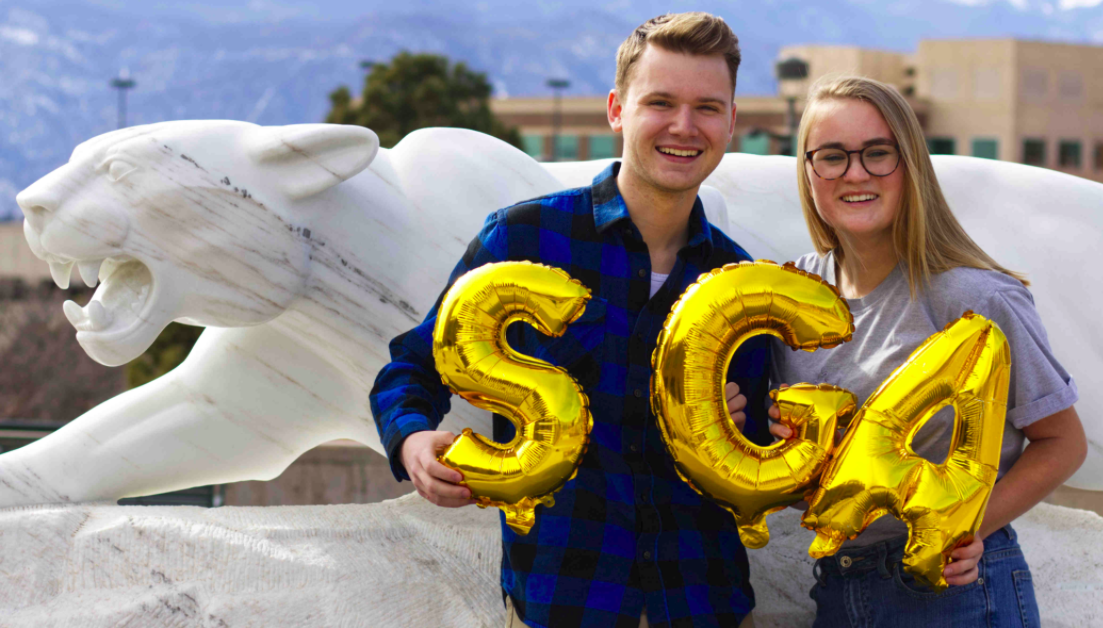 Photo of Aidan Meadows and Rachel Cauwels standing in front of the mountain lion statue on campus.