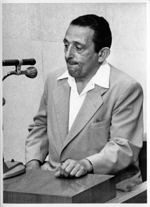 Henryk Ross testifica durante el proceso de Adolf Eichmann. Además de sus responsabilidades como fotógrafo del Departamento de Estadísticas del ghetto de Lodz, Ross secretamente fotografió escenas en el ghetto. A la derecha de Ross está el fiscal general Gideon Hausner, que tiene en su mano algunas de las fotografías de Ross presentadas como pruebas