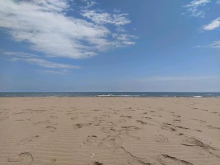 Picture of a beach with sand, the sea and a blue sky with some clouds