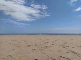 Picture of a beach with sand, the sea and a blue sky with some clouds