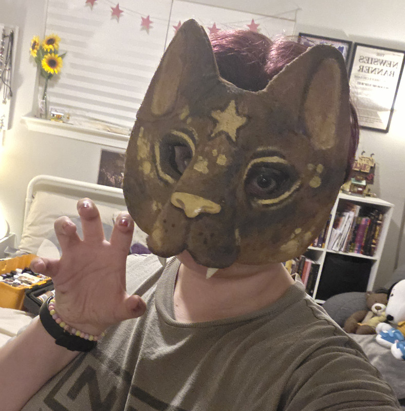3 of 3. The webmaster wearing the mask. It covers the majority of his face, with only his chin visible. His eyes look at the viewer and his hand makes a claw.