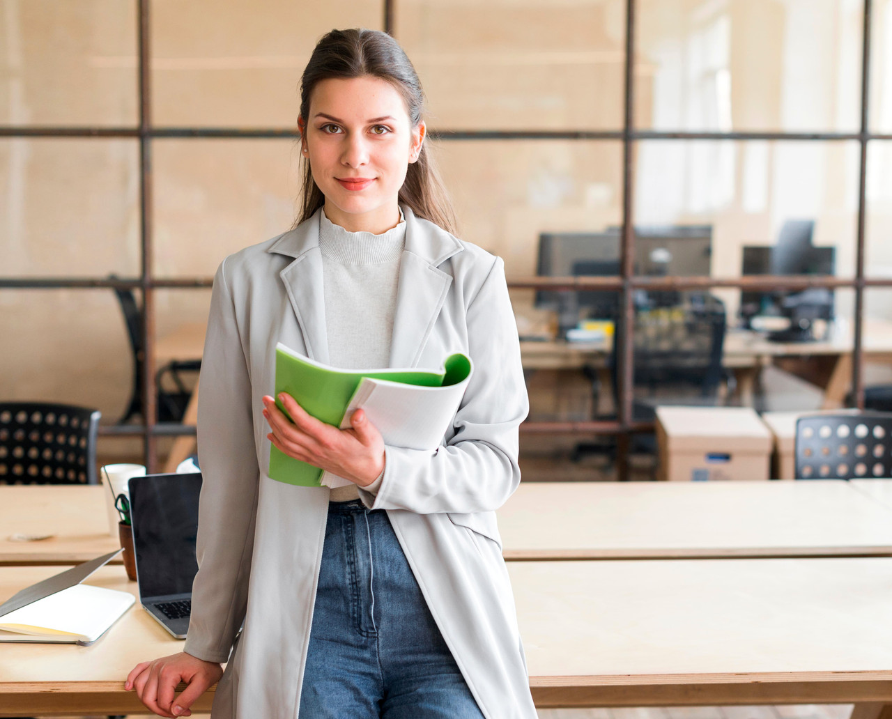 pretty young businesswoman leaning desk holding book looking camera office 4