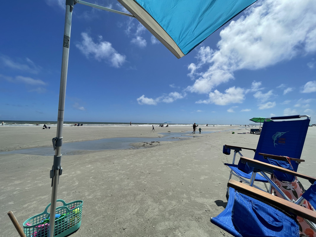 gratuitous beach pic: under an umbrella flag looking out at the beach and ocean. a few folks in the distance and some beach chairs in the foreground