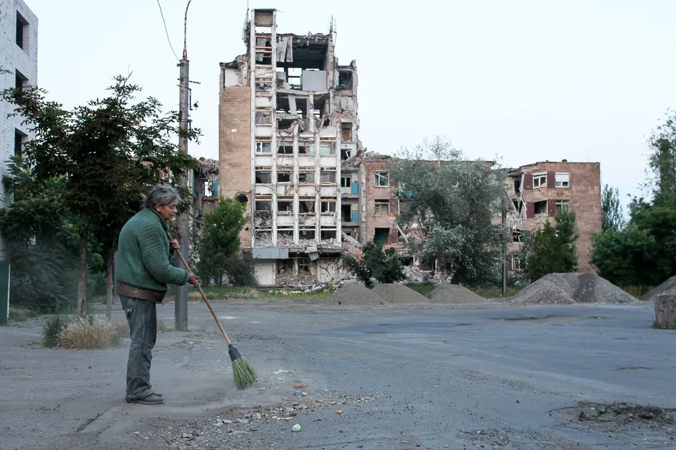 Жительница захваченного Россией Мариуполя убирает улицу на фоне разрушенного жилого дома. 11 июня 2023 года