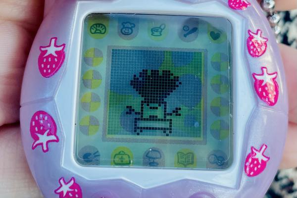 up close photo of a tamagotchi connection device (2024 rerelease) showing ALIBI the robot wearing a big wig that sticks out so high it doubles her height