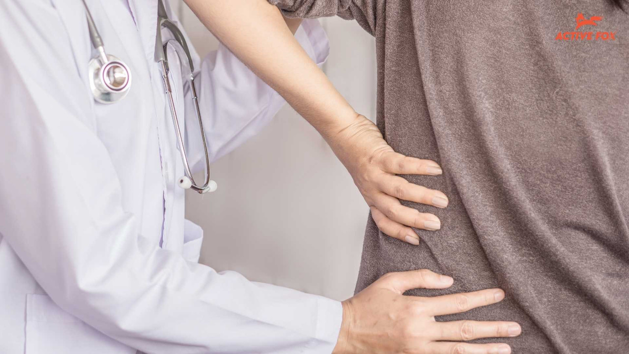 Bác sĩ thăm khám vùng thắt lưng cho bệnh nhân bị đau lưng kéo dài — dấu hiệu cần đi khám chuyên khoa cơ xương khớp — Active Fox