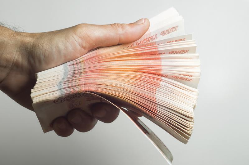 la-main-masculine-tient-une-pile-épaisse-d-argent-liquide-million-de-roubles-russes-le-concept-des-r